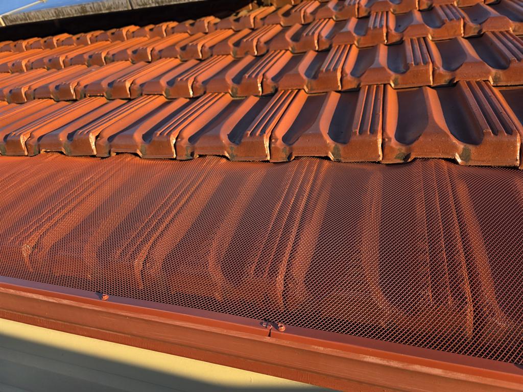 Close-up of terracotta-coloured mesh gutter guard fitted under roof tiles