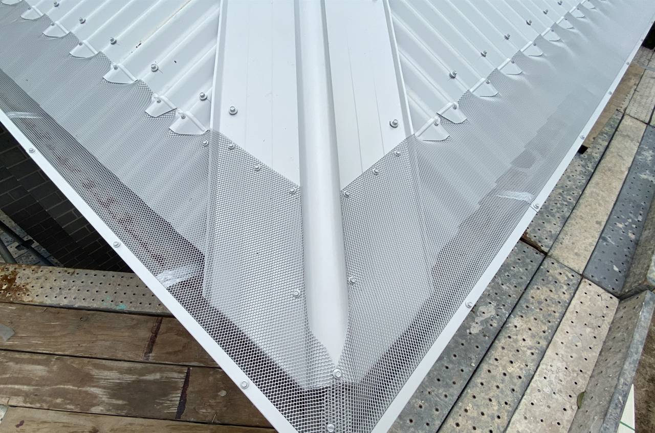Mesh gutter guard covering the hip and valley of a white corrugated roof