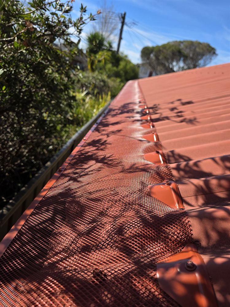 Terracotta-coloured mesh gutter guard along a red roof in dappled shade