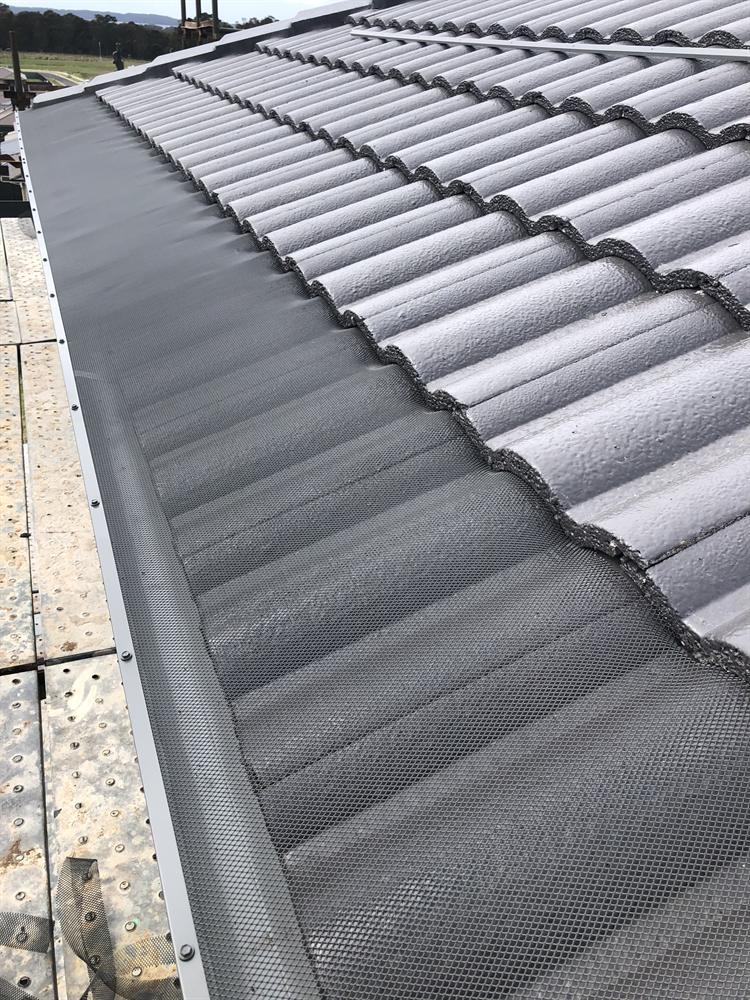 Mesh gutter guard along the edge of a grey concrete tile roof