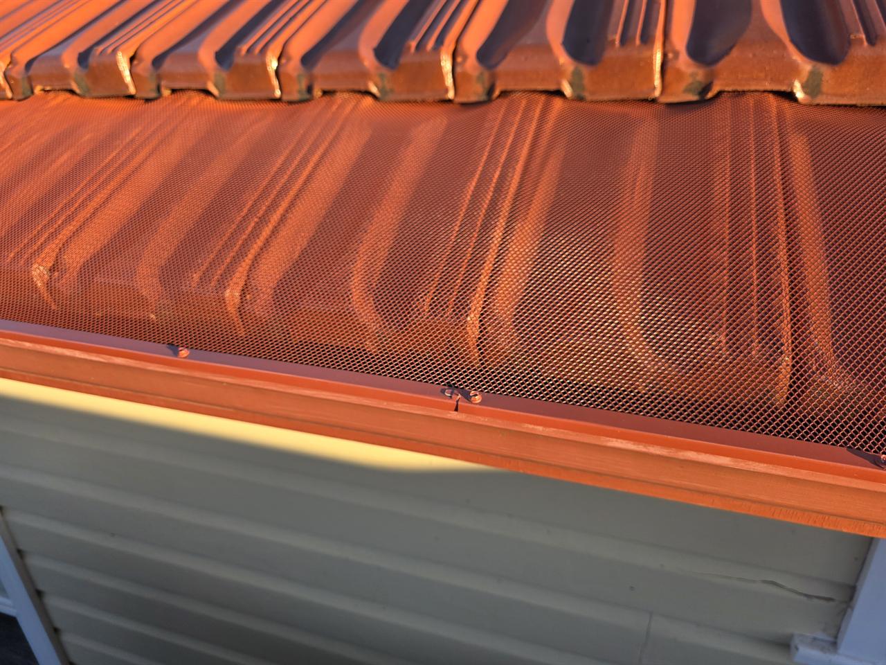 Colour-matched mesh gutter guard over a terracotta gutter, close up