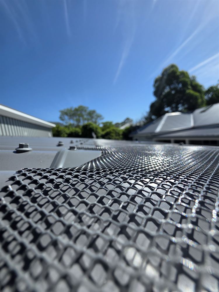 Close-up of aluminium mesh gutter guard on a corrugated roof against a blue sky