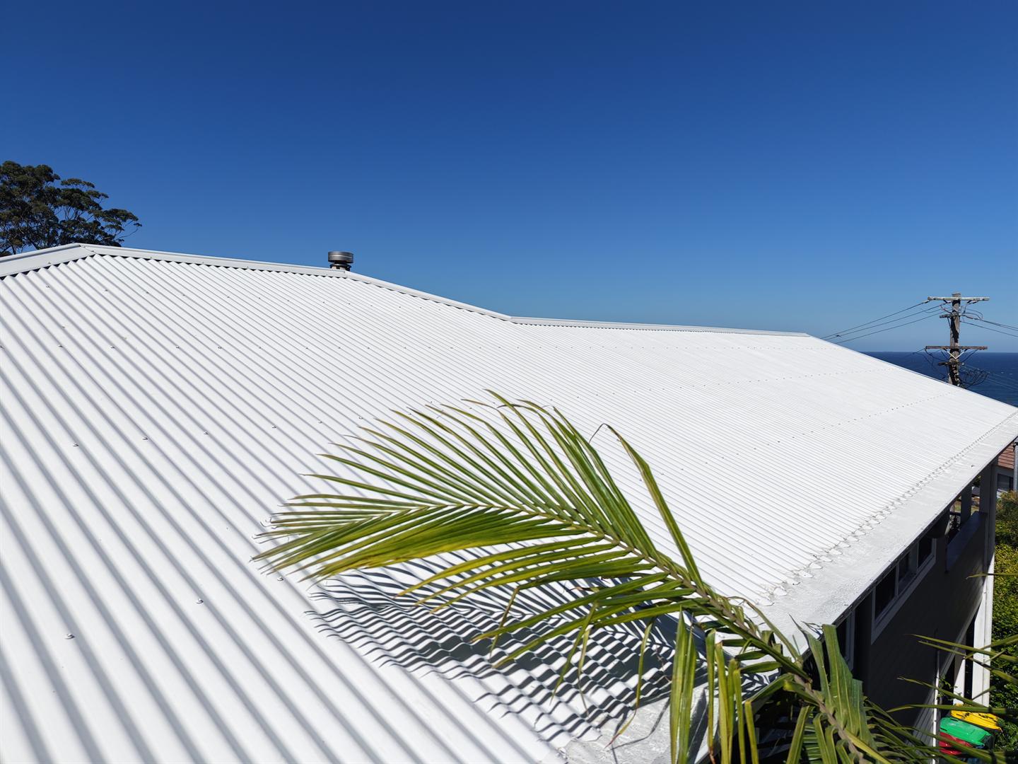 Drone view of a clean white corrugated roof above the ocean in Wombarra